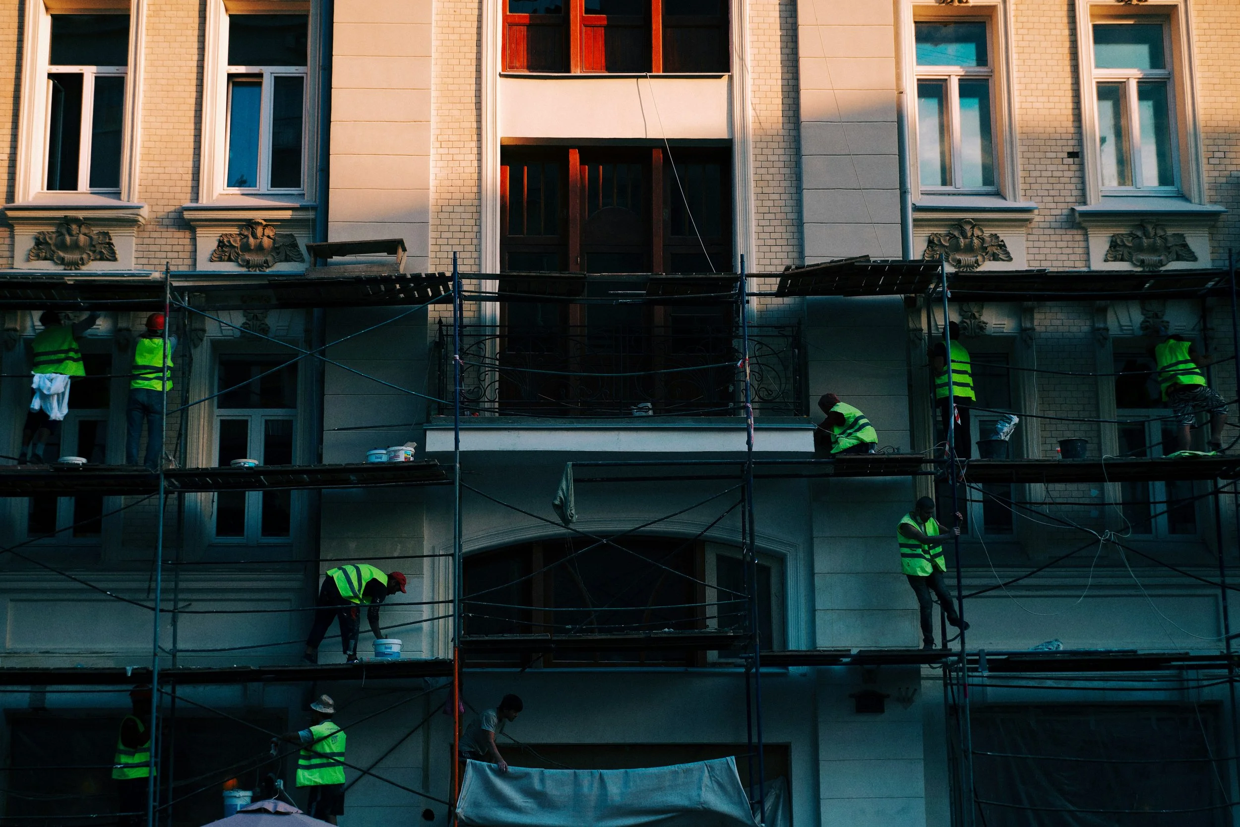 Construction workers in yellow vests working on scaffolding outside a multi-story building.