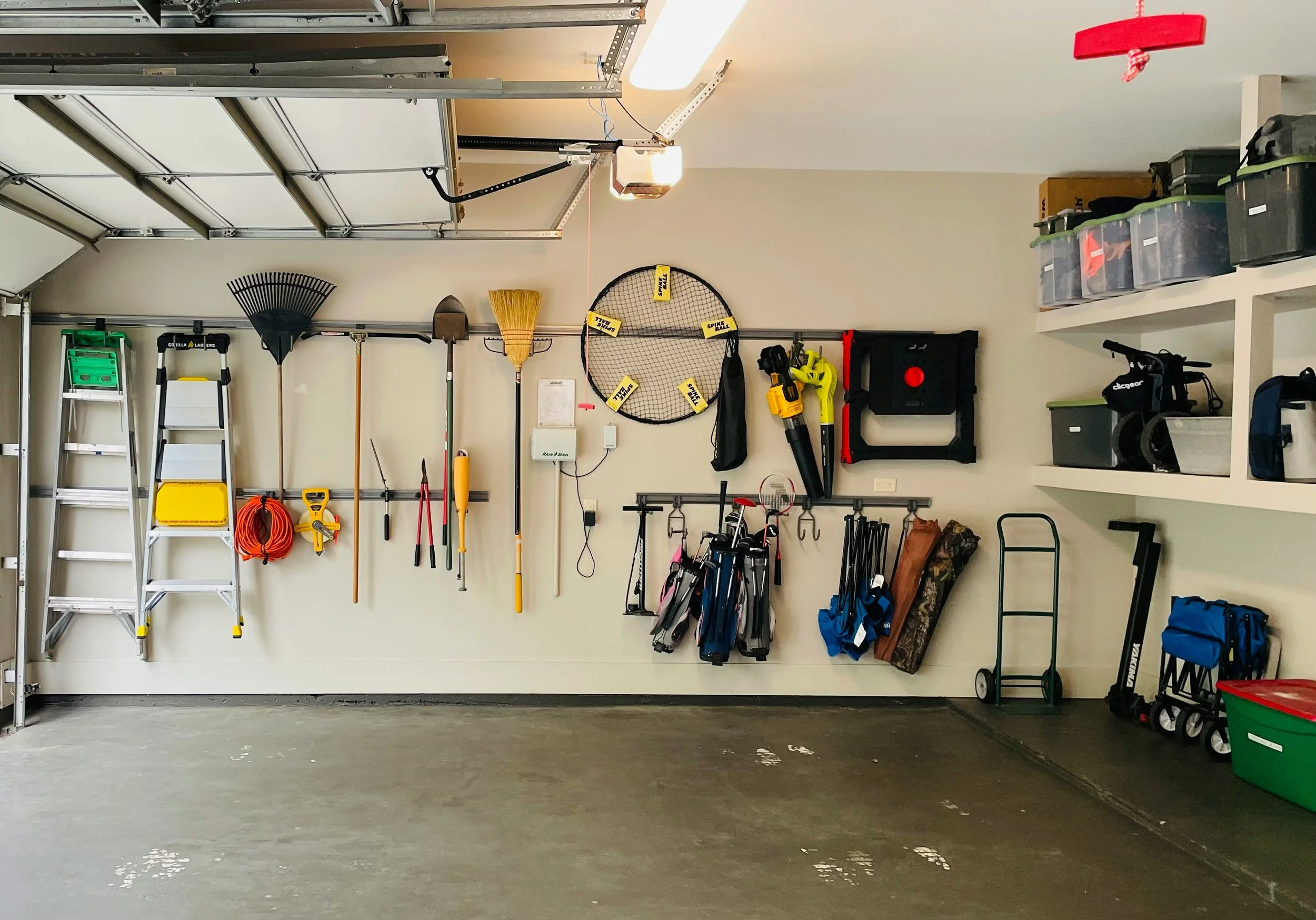 Organized garage with gardening tools, ladders, and storage bins.
