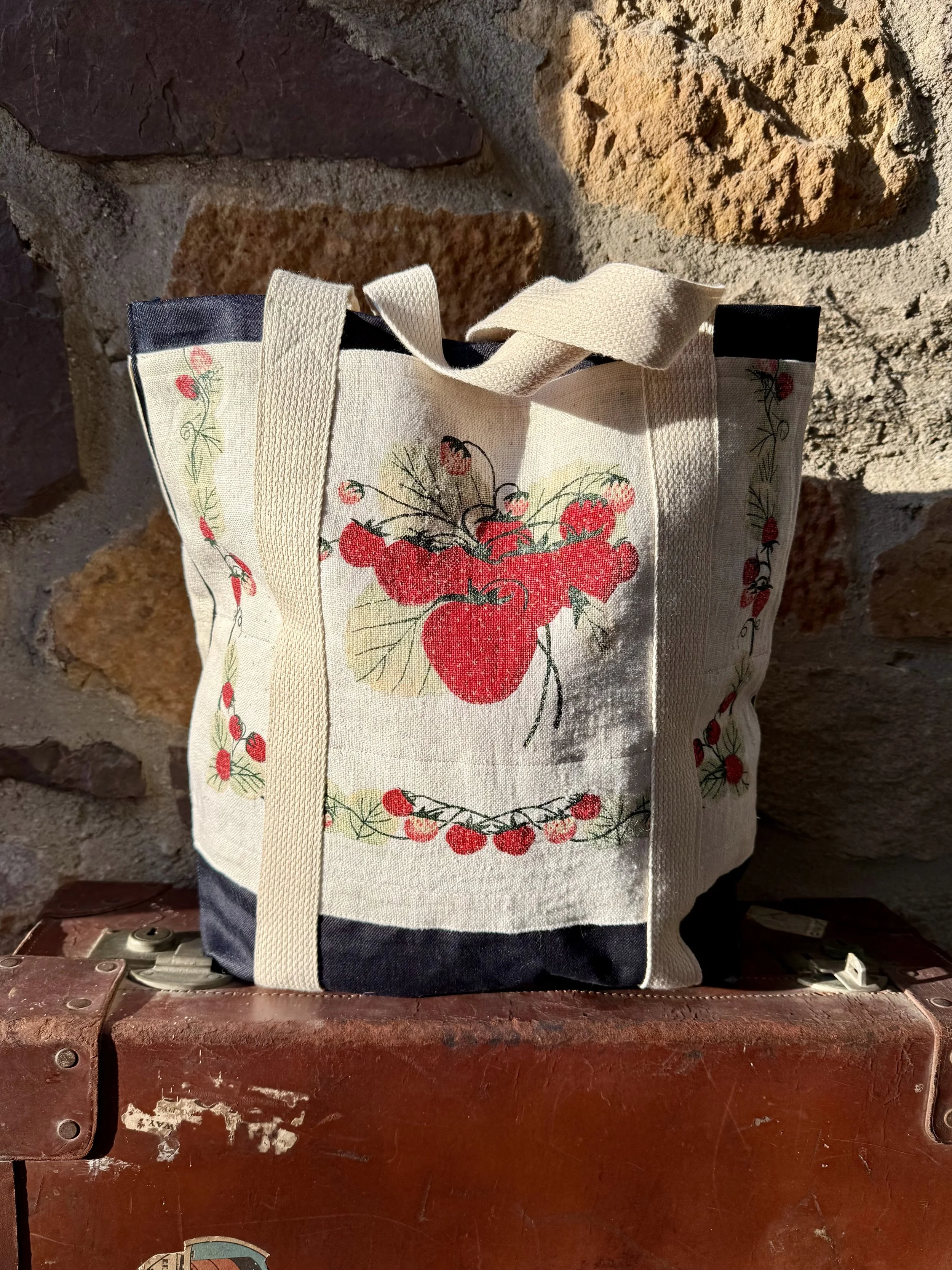 tell him and strawberry tea towel to bag with cotton webbing straps, a top of Vintage suitcase with a stone wall as a background and beautiful fading light