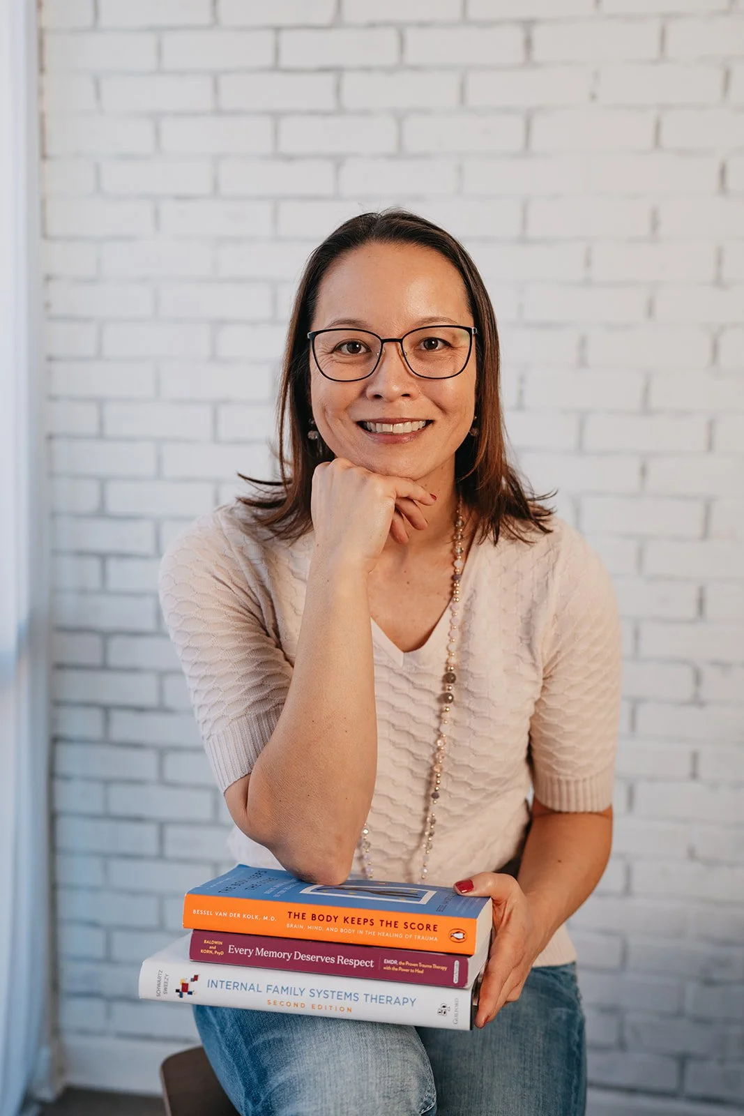Amy Bednarski, Licensed Professional Counselor in Glendale, AZ, warmly smiling with elbow propped up on books.