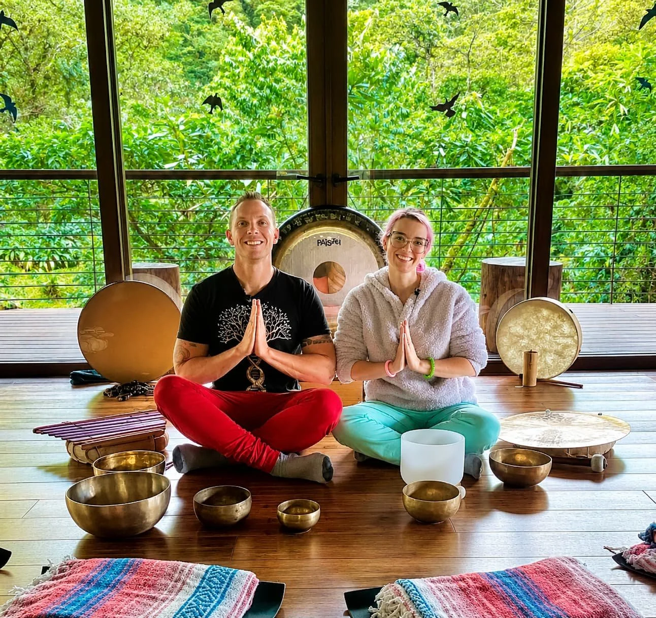 Tieterious and Seraphina Skye sitting with singing bowls and meditation instruments, hands in prayer position, leading a breathwork and sound healing session in Cary NC