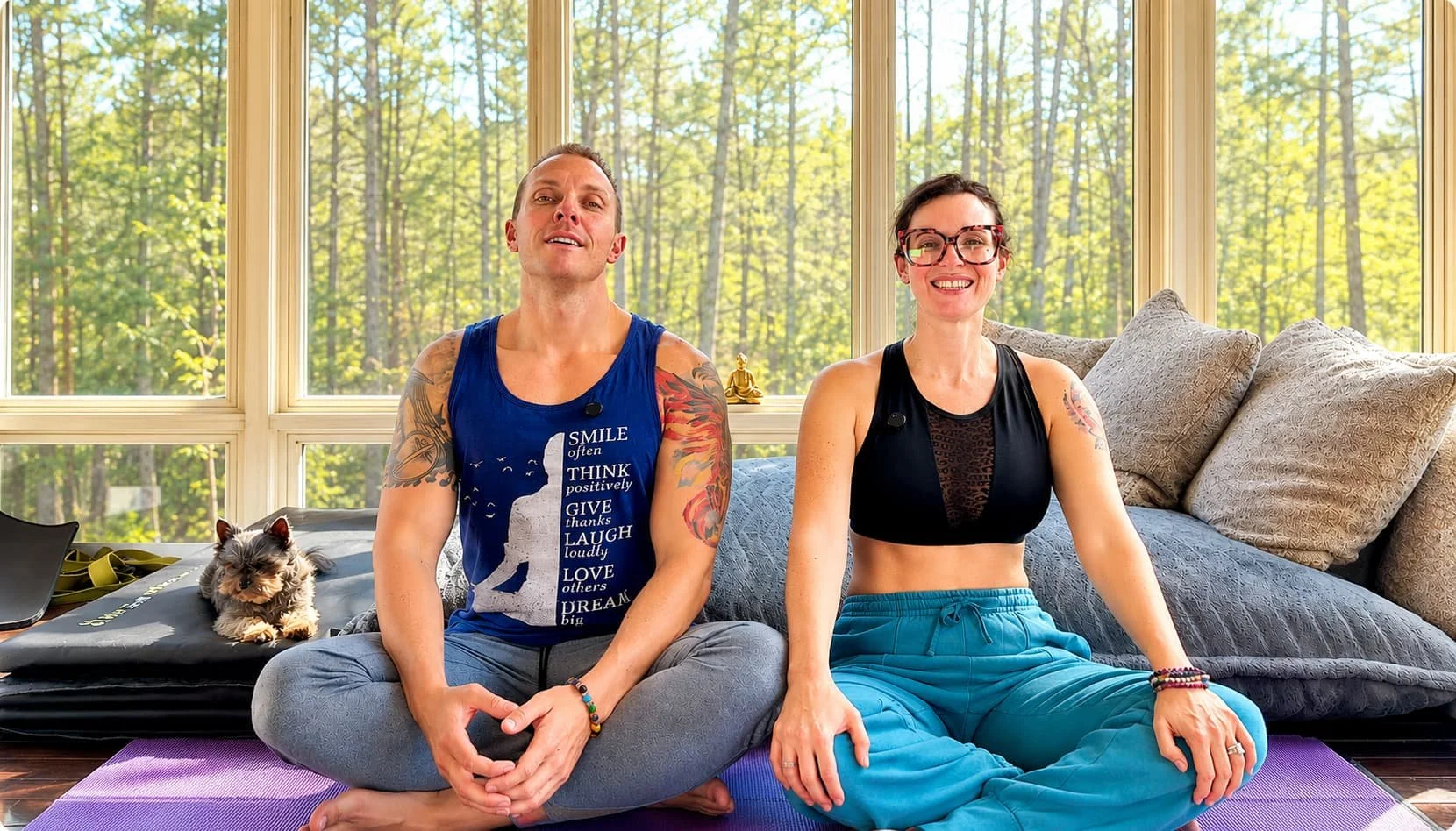 Tieterious and Seraphina Skye sitting on yoga mats in home studio with forest view, smiling together as a couple, certified yoga teachers and breathwork practitioners in Cary NC