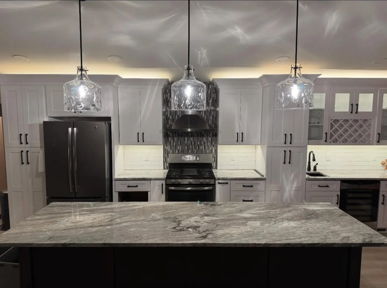 Modern kitchen with gray cabinets, a black refrigerator, a black stove with a stainless steel hood, and a marble countertop kitchen island.