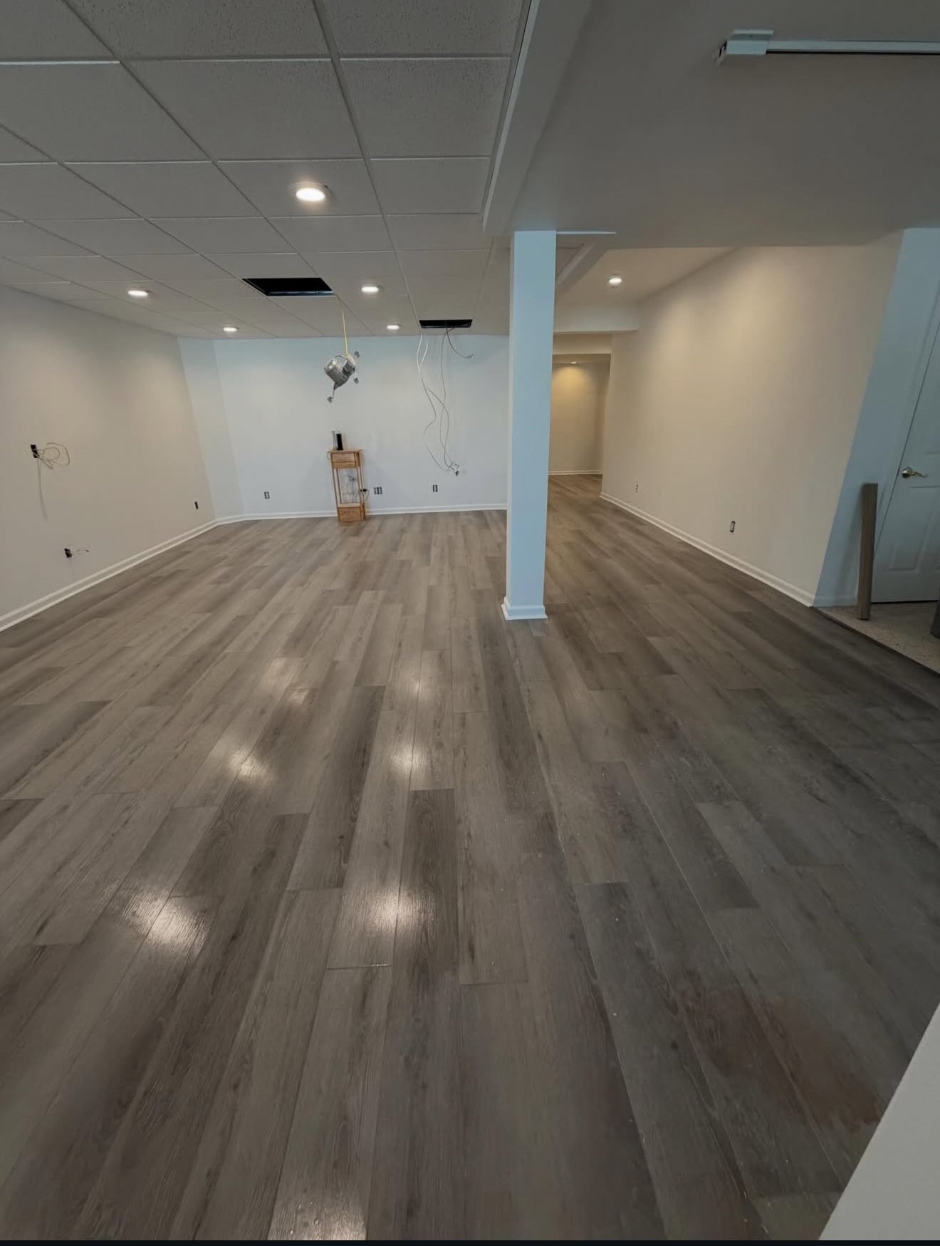 Empty room with partially finished ceiling, installed hardwood flooring, white walls, and some exposed wires hanging from the ceiling.