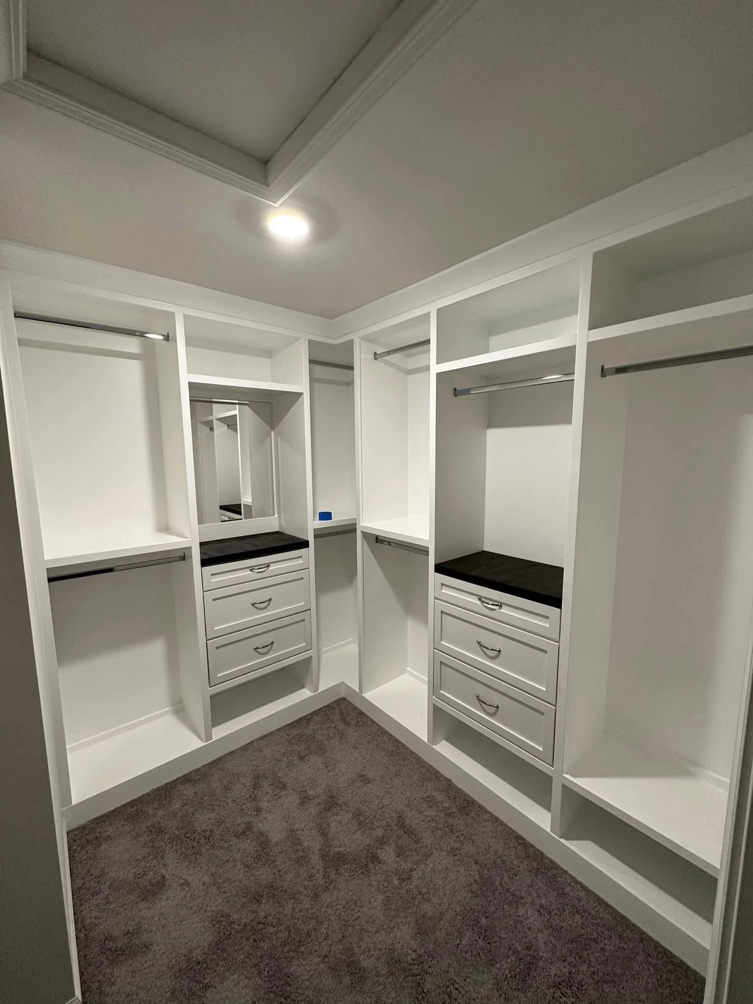 Empty walk-in closet with white built-in shelves, drawers, and hanging rods, brown carpeted floor, and ceiling recessed lighting.