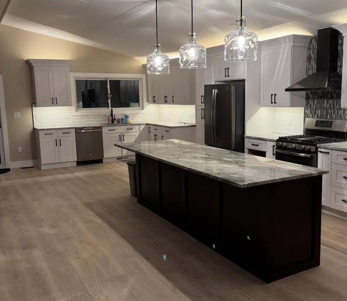 Modern kitchen with white cabinets, a large dark island with a marble countertop, stainless steel appliances, and three pendant lights hanging above the island.