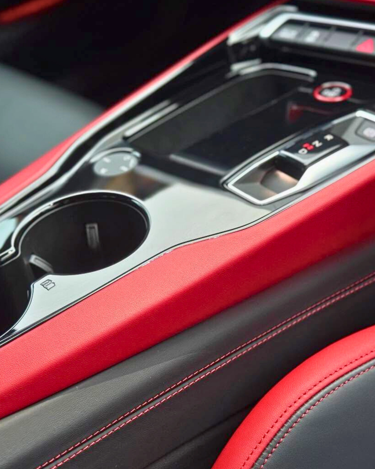 Close-up view of a pristinely clean car's center console with red and black leather upholstery, a cup holder, and gear shift with a red marking.