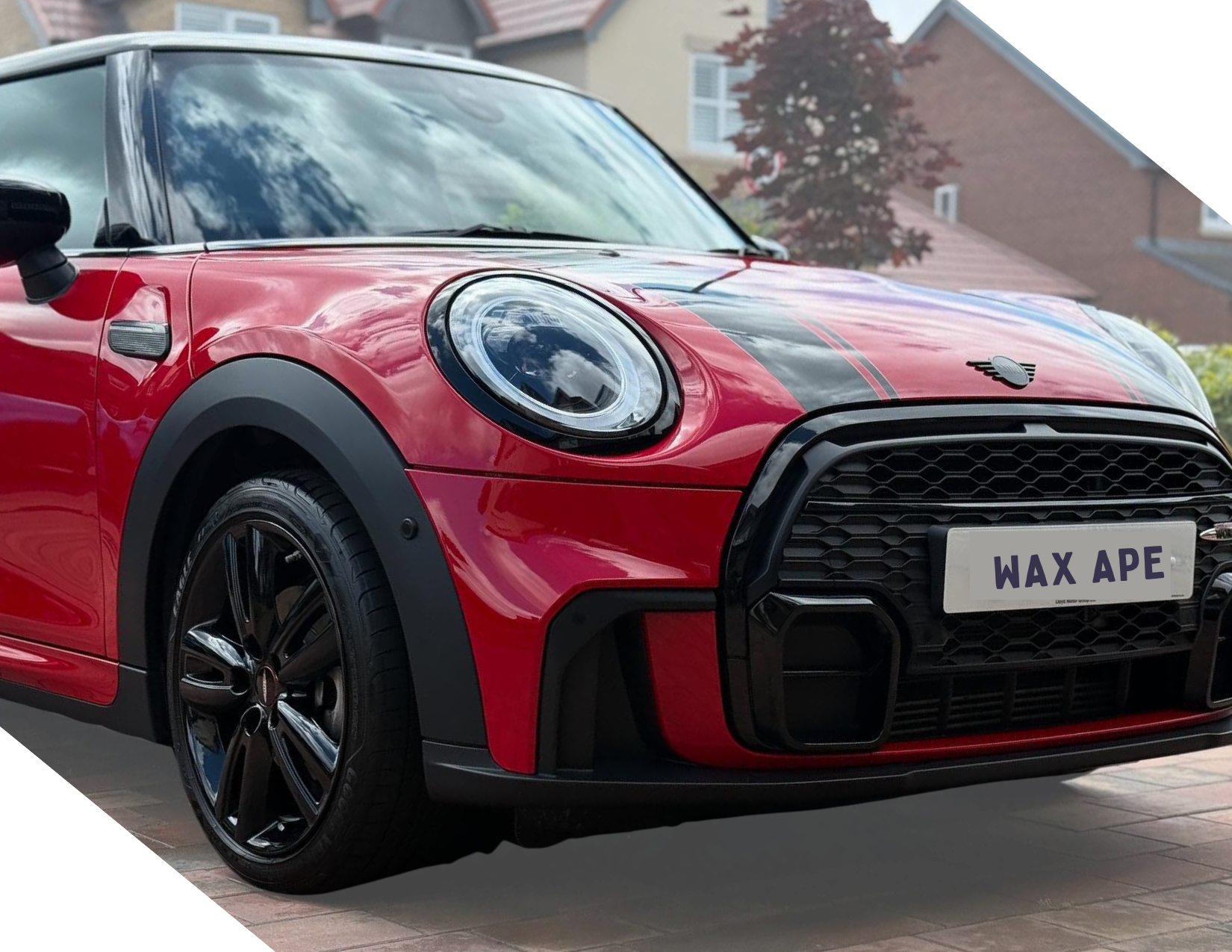 A pristine, shiny clean red compact car with black accents parked on a residential driveway, with a building and trees in the background.