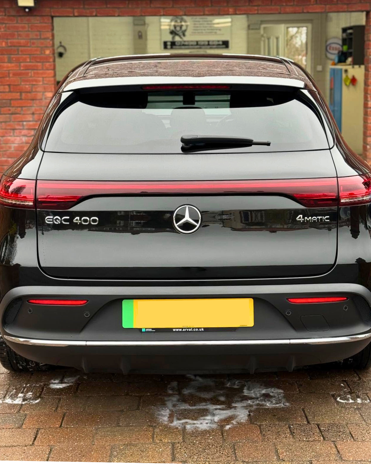 Rear view of a newly detailed black Mercedes-Benz EQC 400 electric car parked on a brick driveway.  The shiny finish reflects the surroundings.