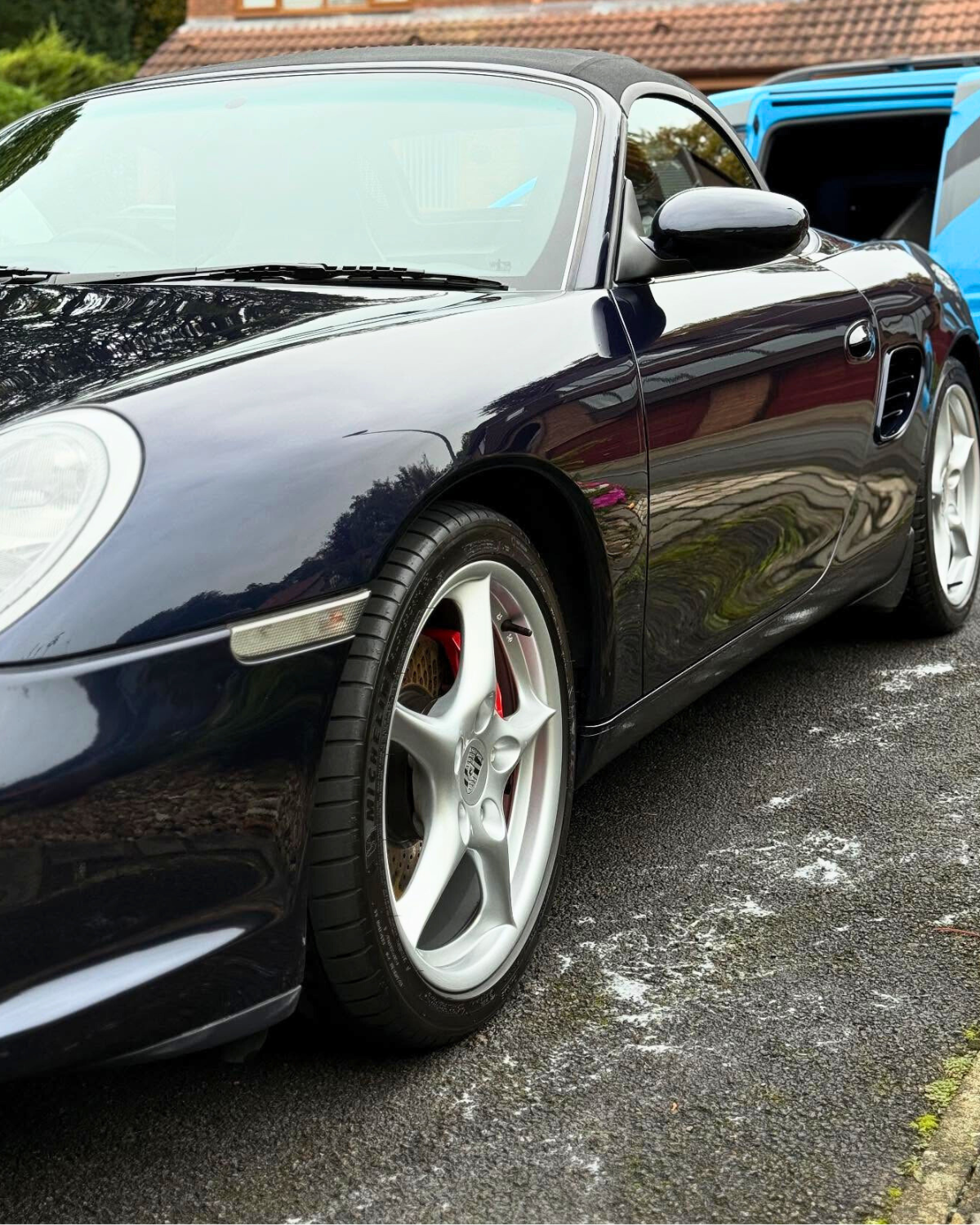 Black Porsche convertible, with pristinely shiny paint parked on driveway with white wheels, visible Porsche logo, and red brake calipers.