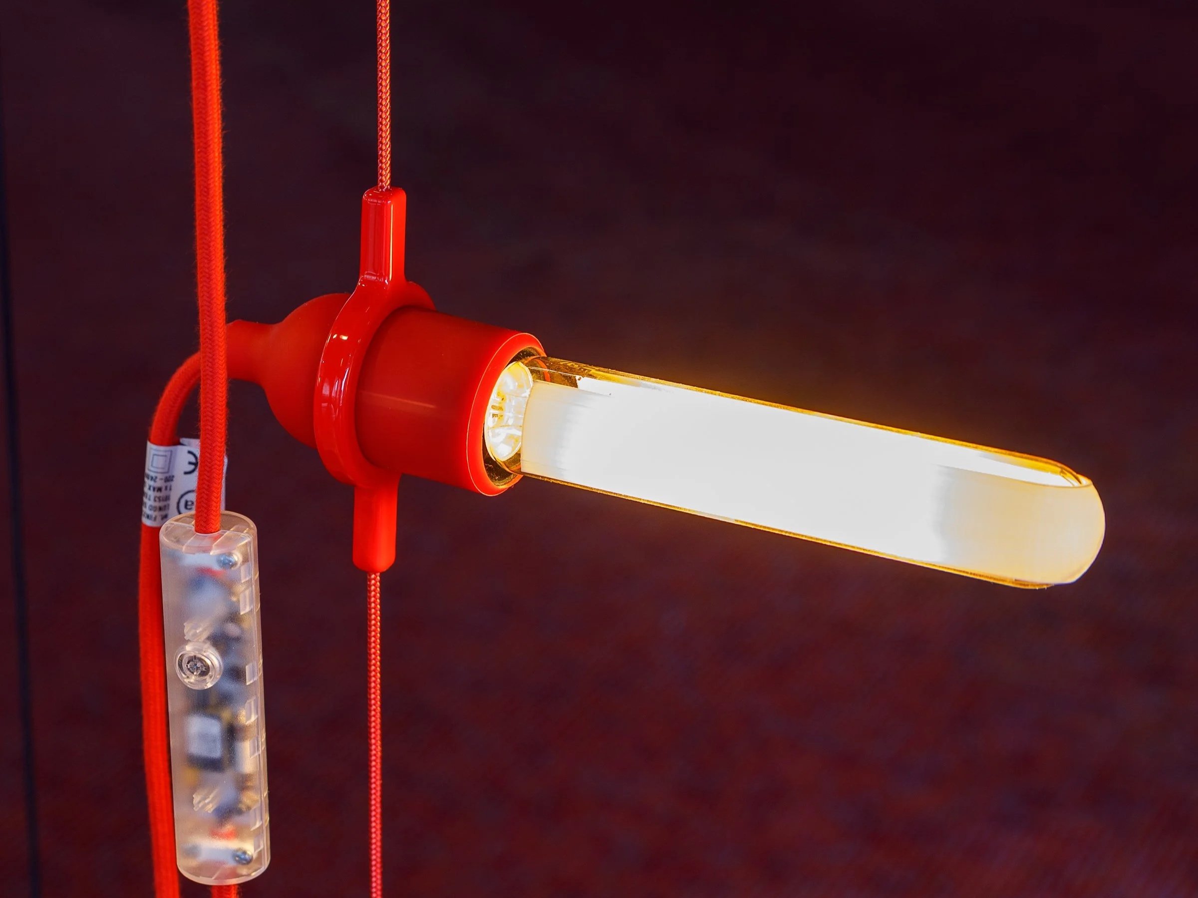 Close-up of an orange and red industrial LED work light with a bright white light, attached to red cords and a transparent control box.