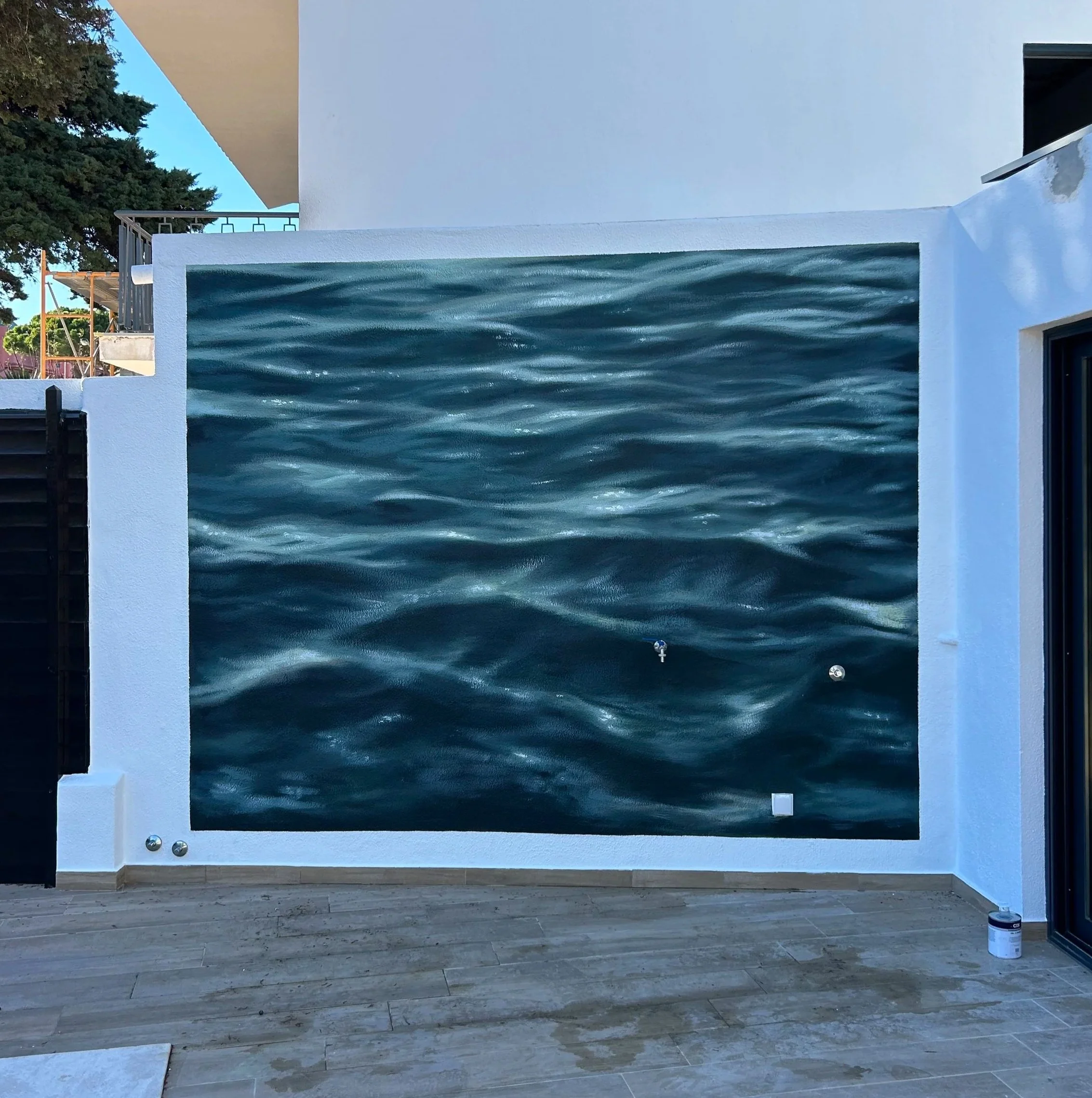 A mural of ocean water with ripples is painted on the exterior wall of a building, creating a realistic water scene.