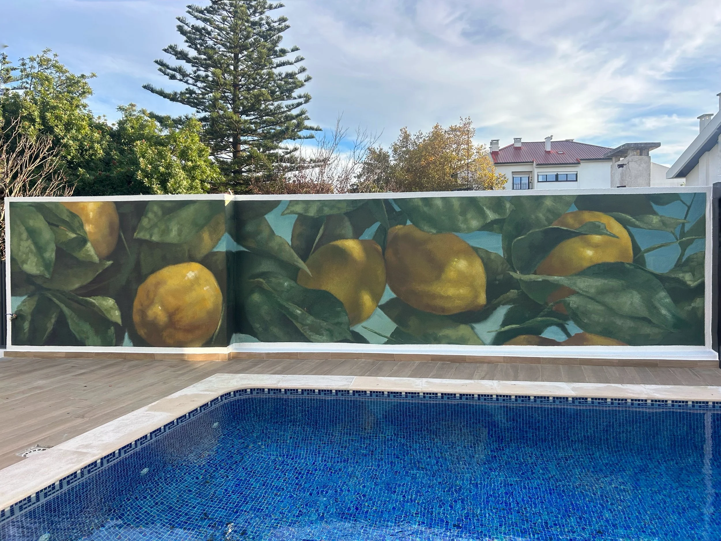 A mural of yellow lemons with green leaves painted on a wall behind a swimming pool.