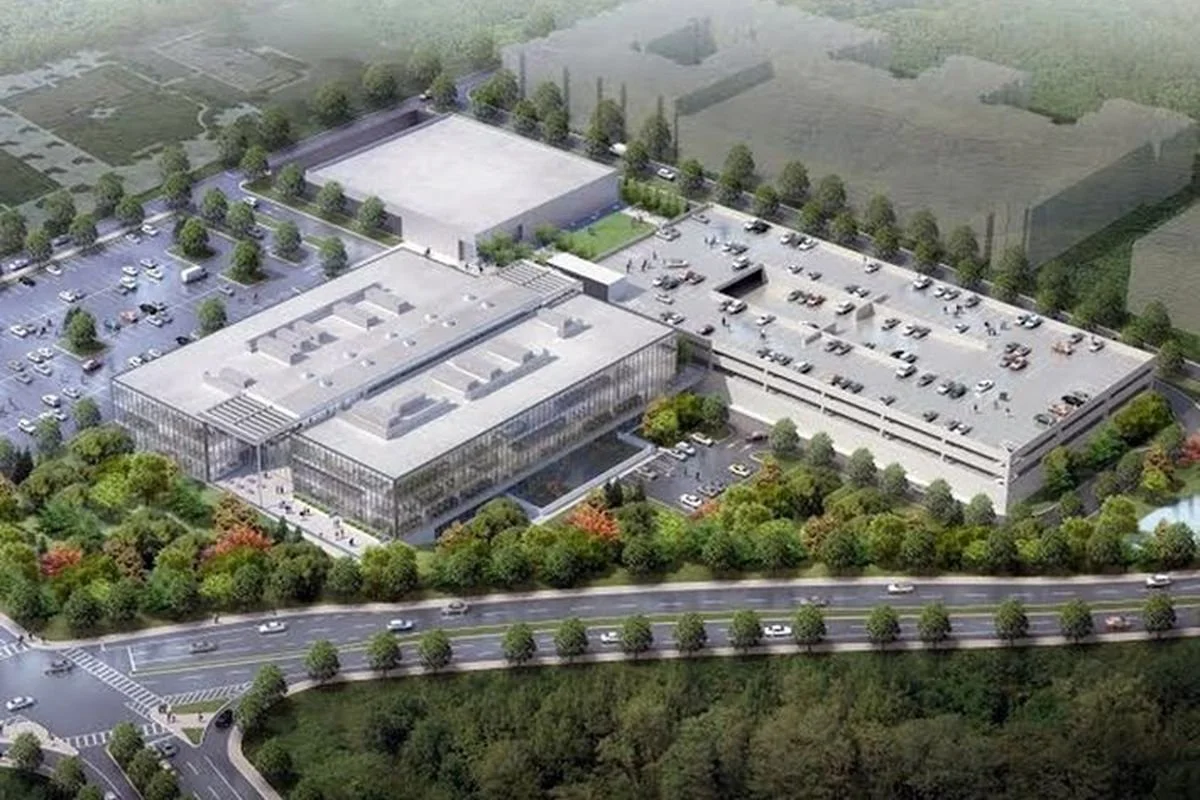 An aerial view of a large modern building complex with multiple parking lots, surrounded by trees and greenery.