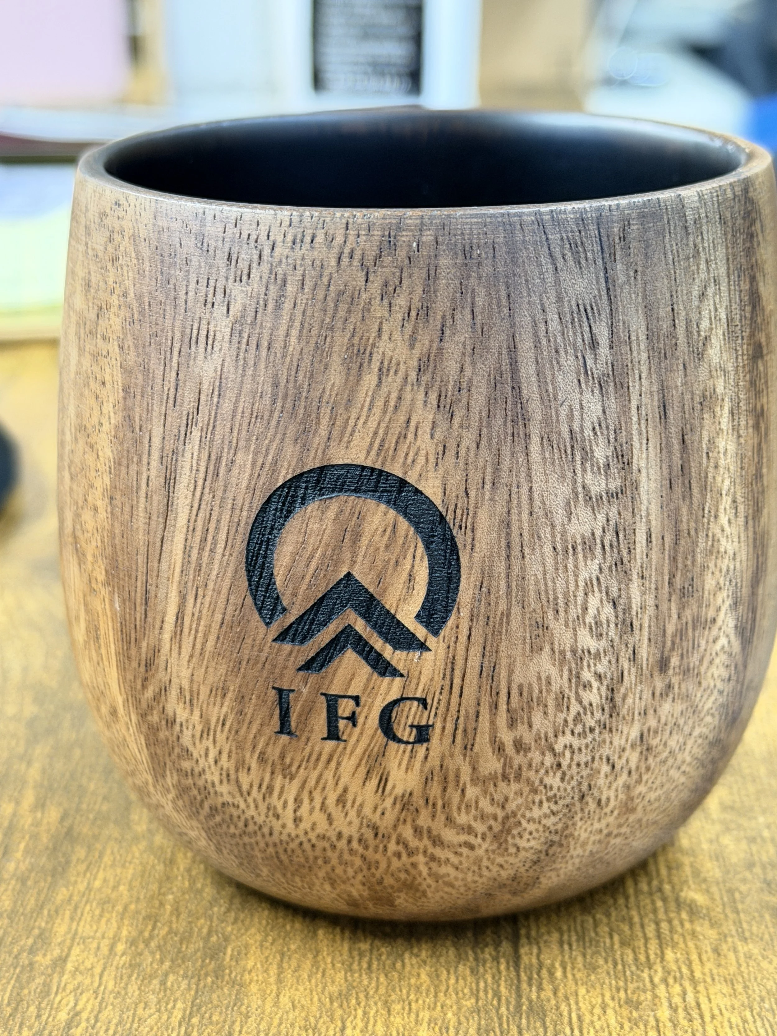 A wooden mug with a black interior and an engraved logo with the letters 'IFG' on the front.
