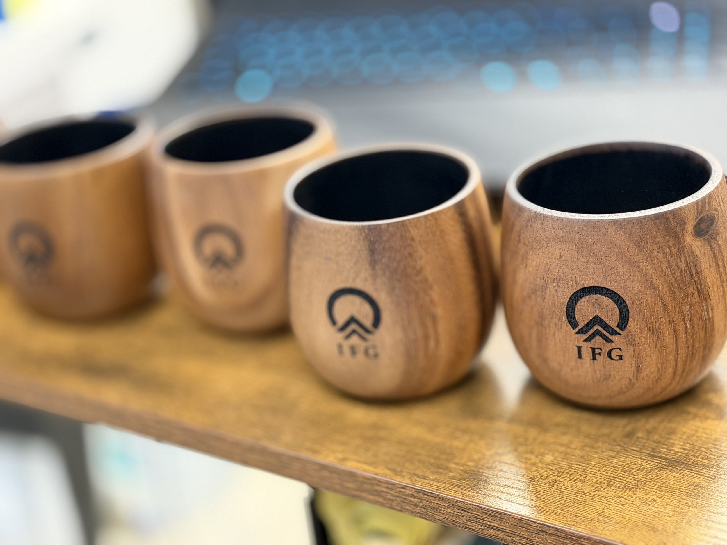 Four wooden cups with black interior and logo on front, placed on a wooden surface.