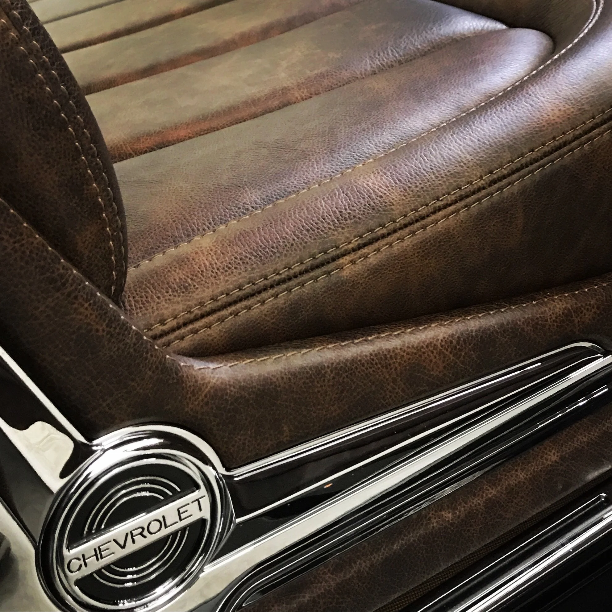 Close-up of a vintage Chevrolet car seat with brown leather upholstery and chrome Chevrolet emblem on the side.