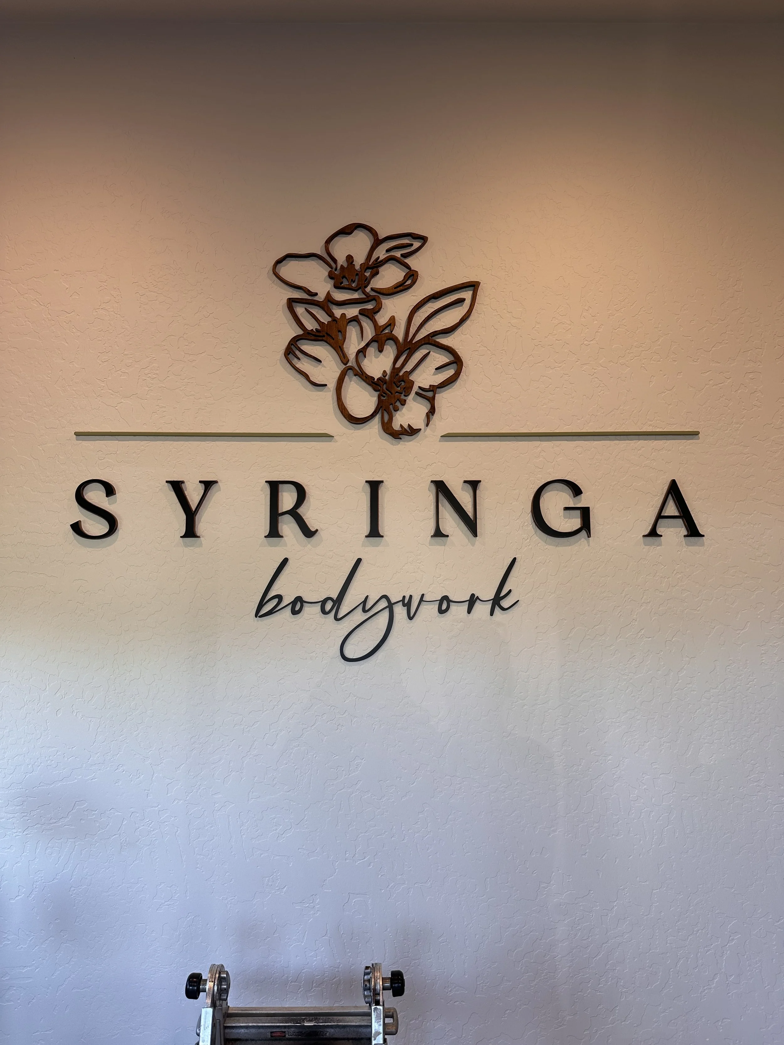 Interior wall with a sign that says 'SYRINGA bodywork' and a decorative floral design above the text.