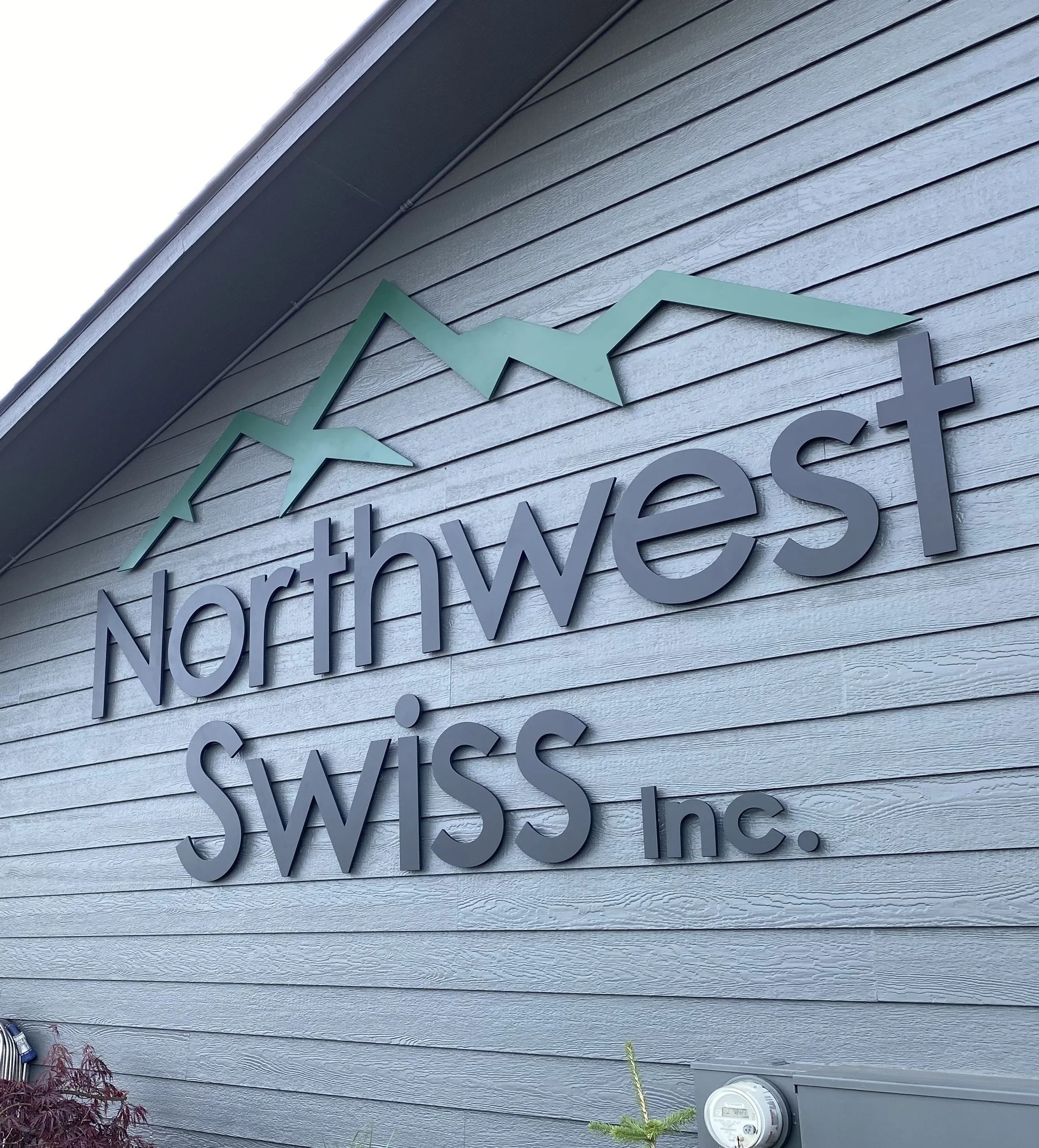 A sign on a building with the words 'Northwest Swiss Inc.' and a mountain range graphic above.