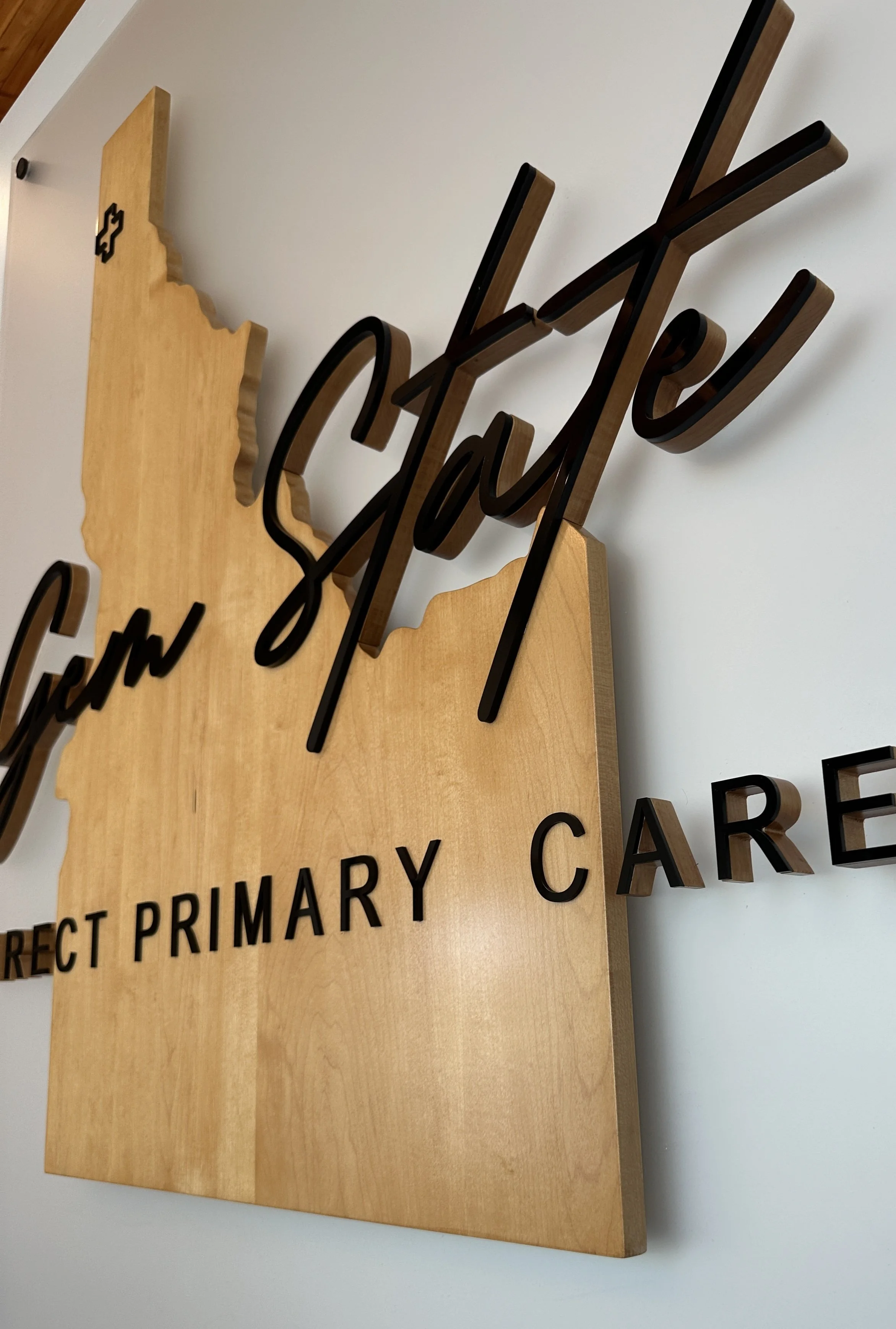 Wooden sign with black cursive and capital letters, featuring an outline of the state of Idaho and the phrase 'Geno Jeltz, Direct Primary Care'.