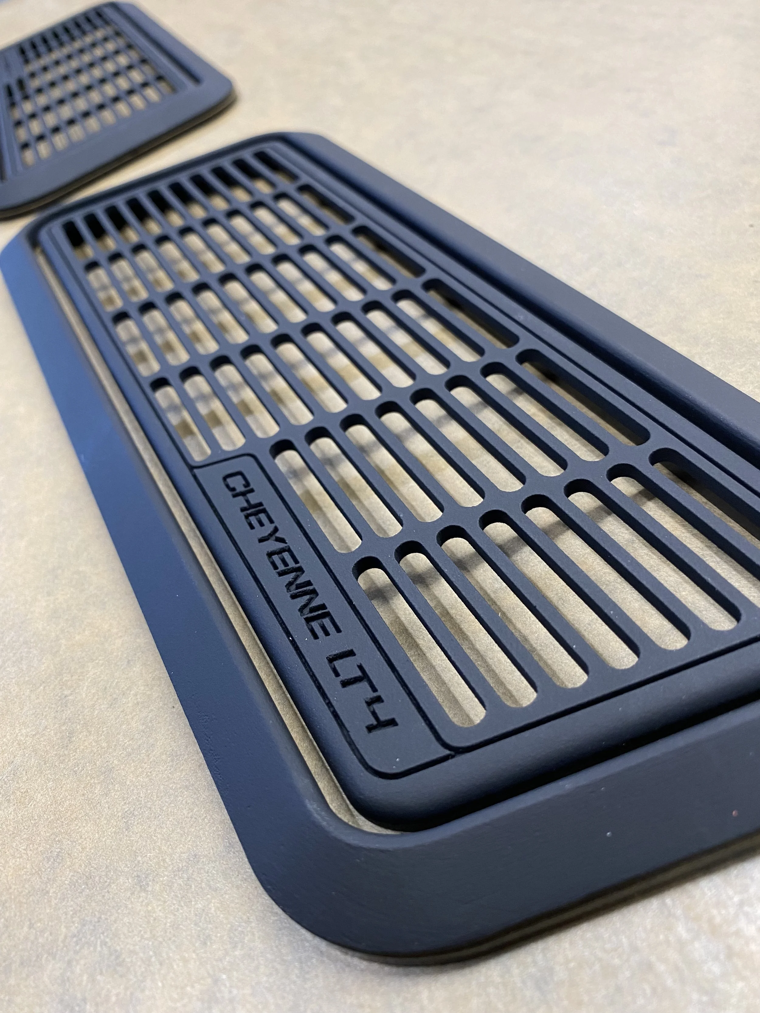 Close-up of a rectangular black rubber grip with parallel slats and the word "CHEYENNE LT 4" engraved on it, placed on a beige surface.