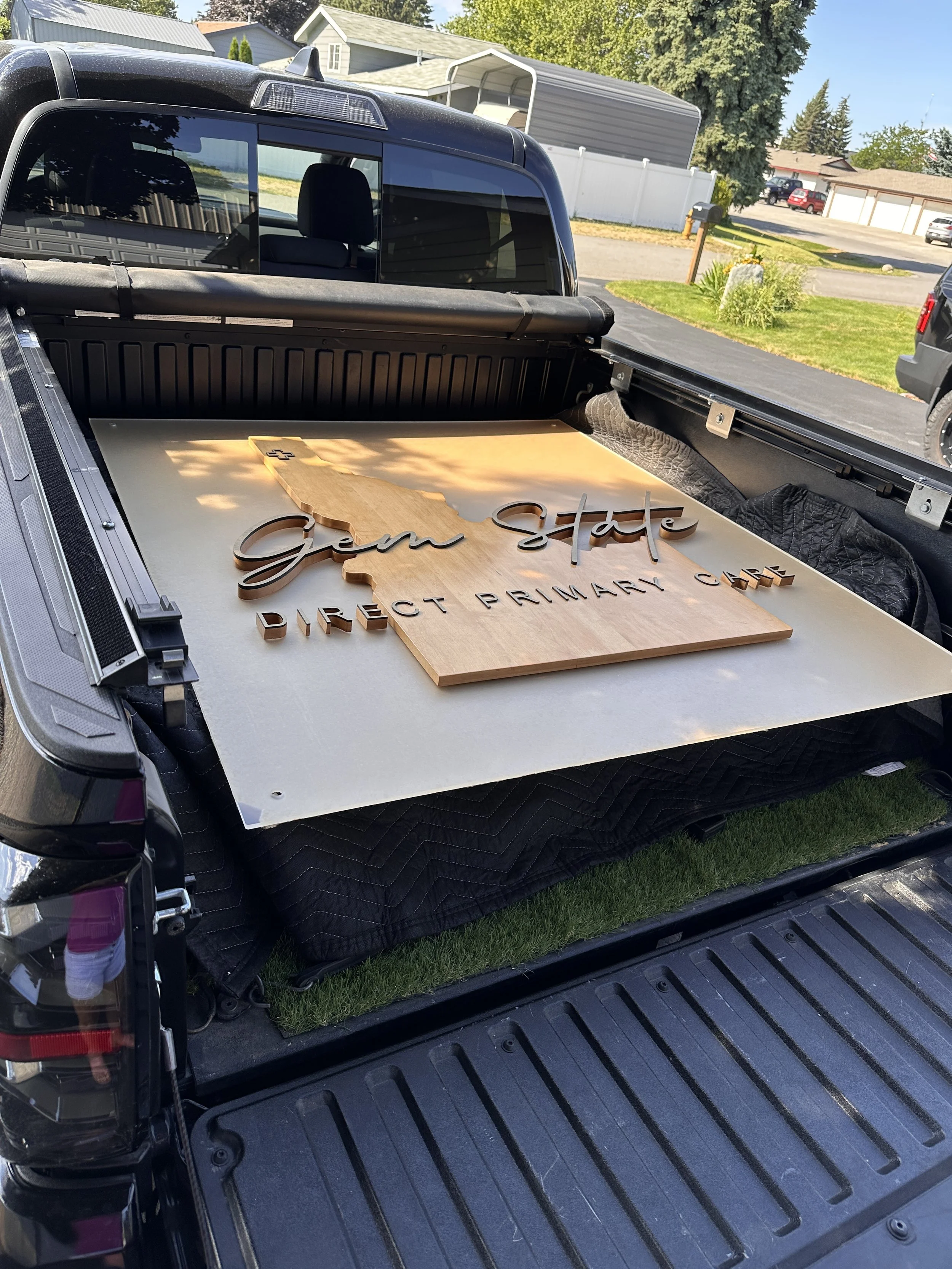 A wooden sign in a truck bed reading 'Gem State' with an outline of the state of Idaho, and 'Direct Primary Care' underneath.
