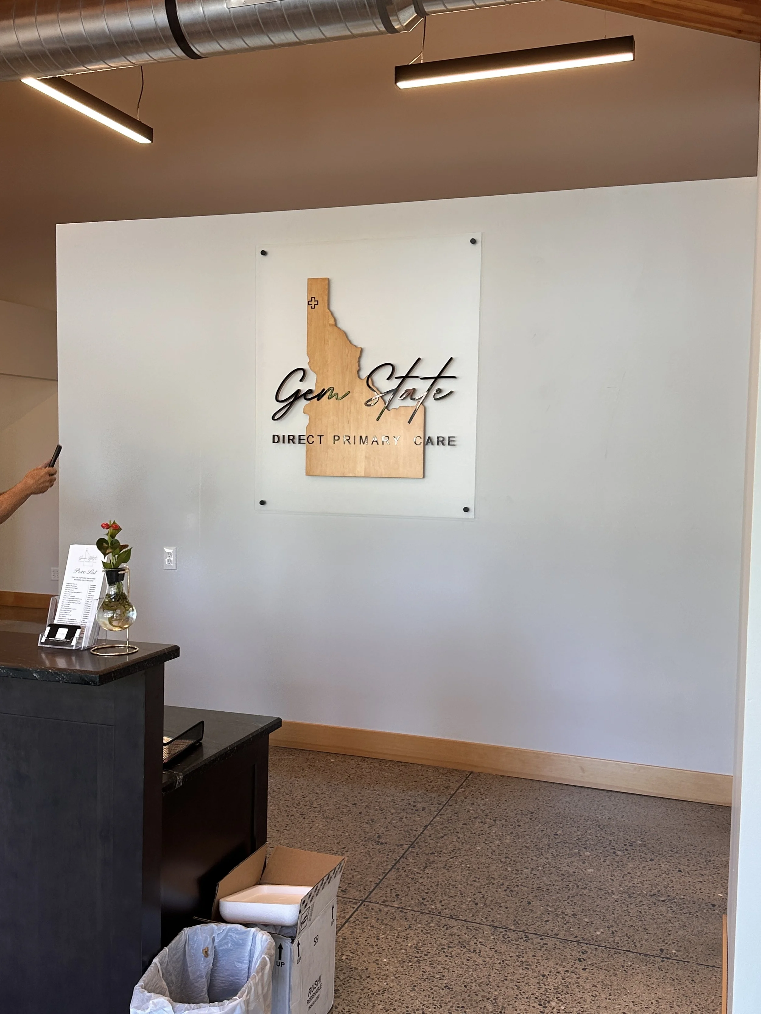 Interior of a medical office with a sign on the wall that reads 'Gem State Direct Primary Care,' featuring a wooden outline of Idaho.