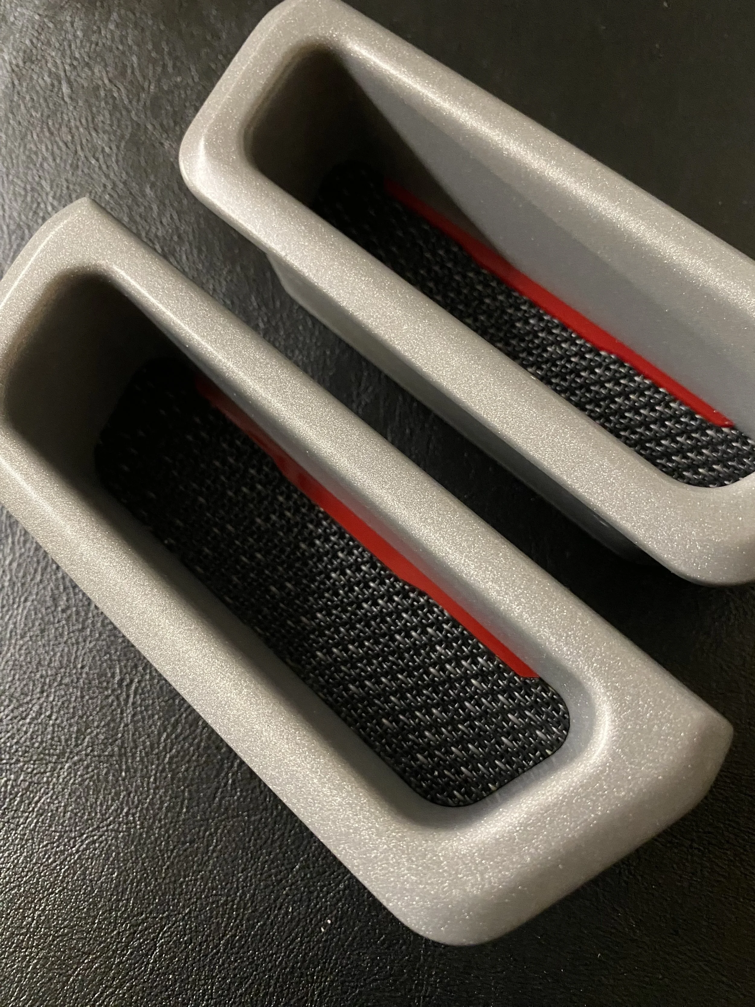 Close-up of two rectangular, gray, textured objects with black elastic bands inside, placed on a black surface.