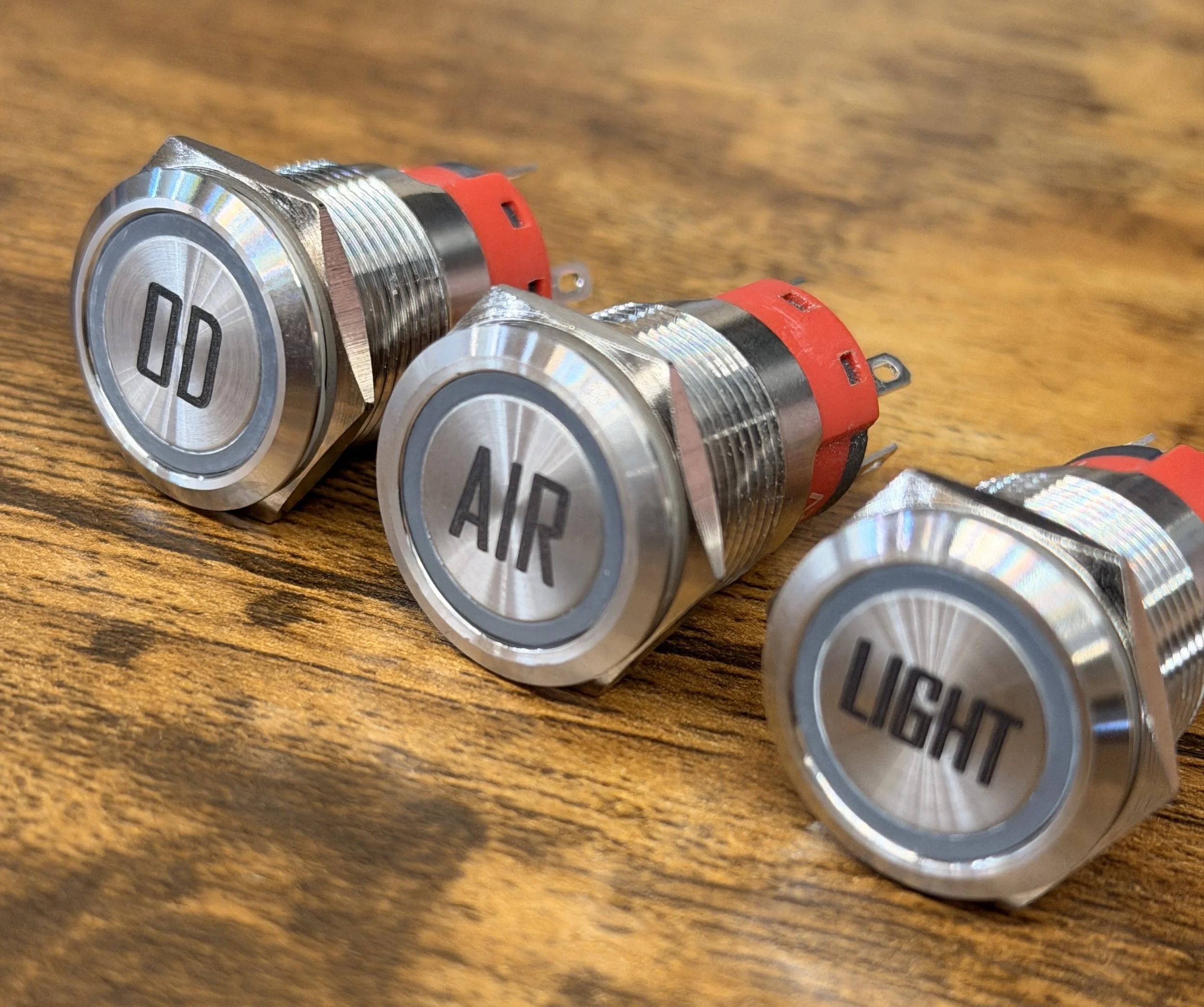 Three metallic push-button switches labeled 'LIGHT', 'AIR', and 'OFF' placed on a wooden surface.