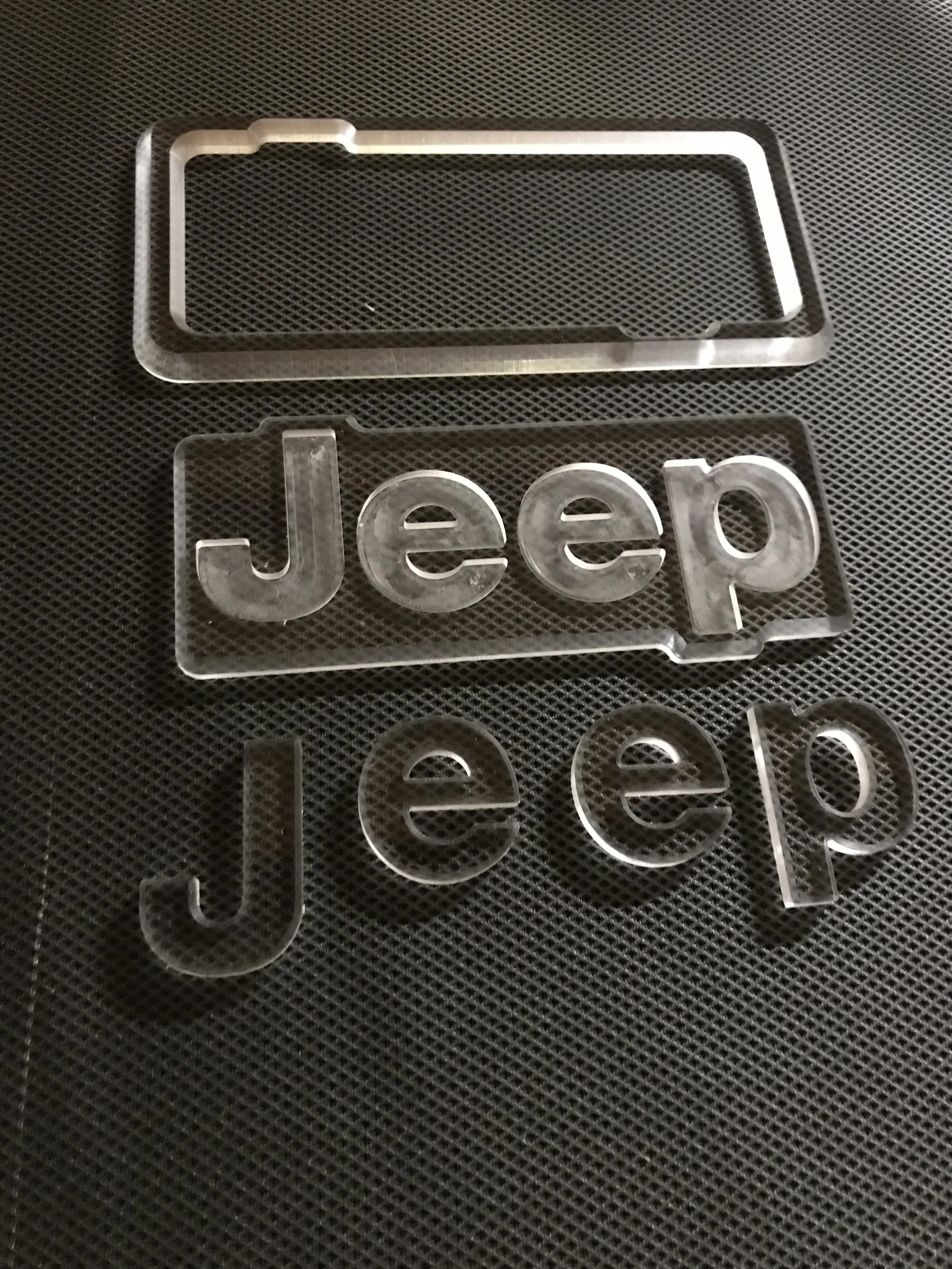 Clear acrylic cutouts of the Jeep logo and a rectangular frame on a black textured surface.