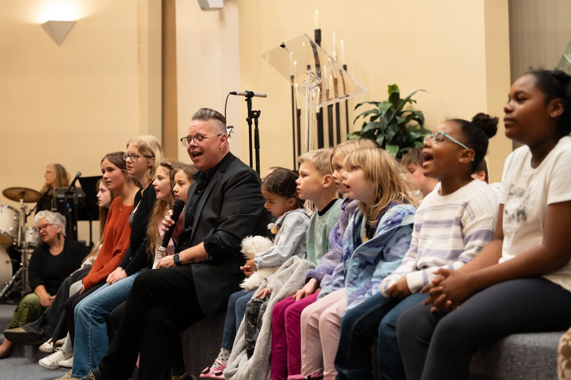 The music director singing while sitting with many ages of kids on stage