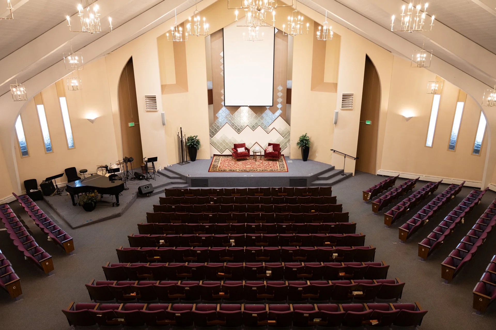 Large auditorium with stage, projector screen, and rows of red seats