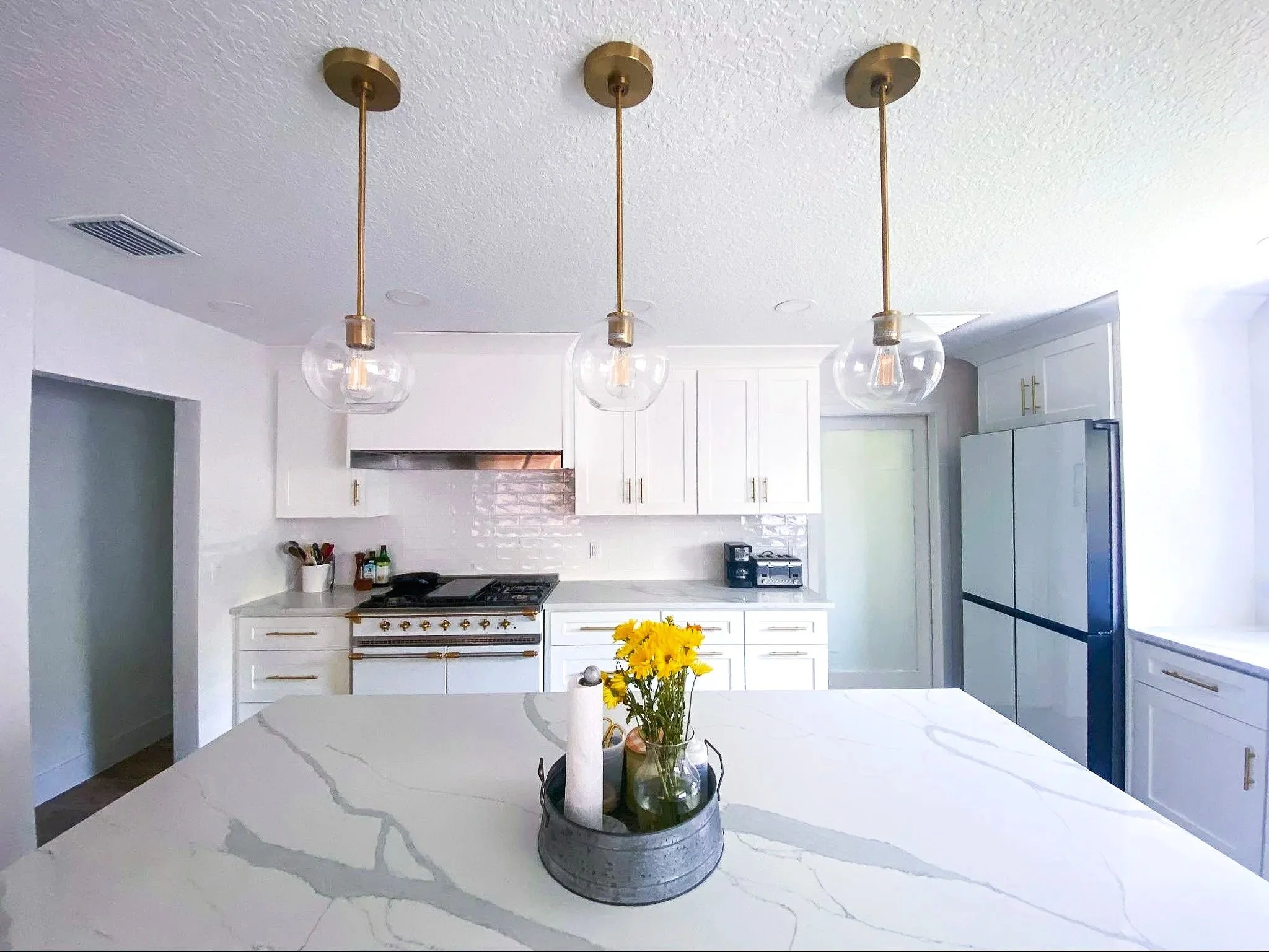 Modern kitchen with white cabinets, a gas stove with brass accents, and a kitchen island with a bouquet of yellow flowers in a gray pot.