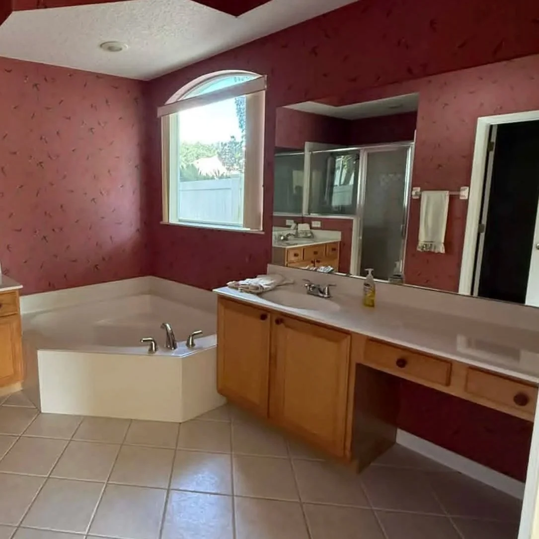 Outdated Orlando primary bathroom with large soaking tub, dual vanities, builder-grade cabinetry, tiled flooring, and dated red accent walls ready for modern renovation.
