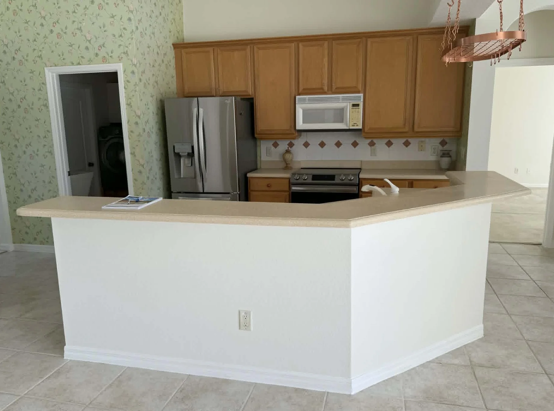 Before renovation, this Orlando-area kitchen featured a dated closed-concept layout with oak cabinets, laminate countertops, tile flooring, and a raised peninsula separating the kitchen from the living space. The remodel transformed the area into a m
