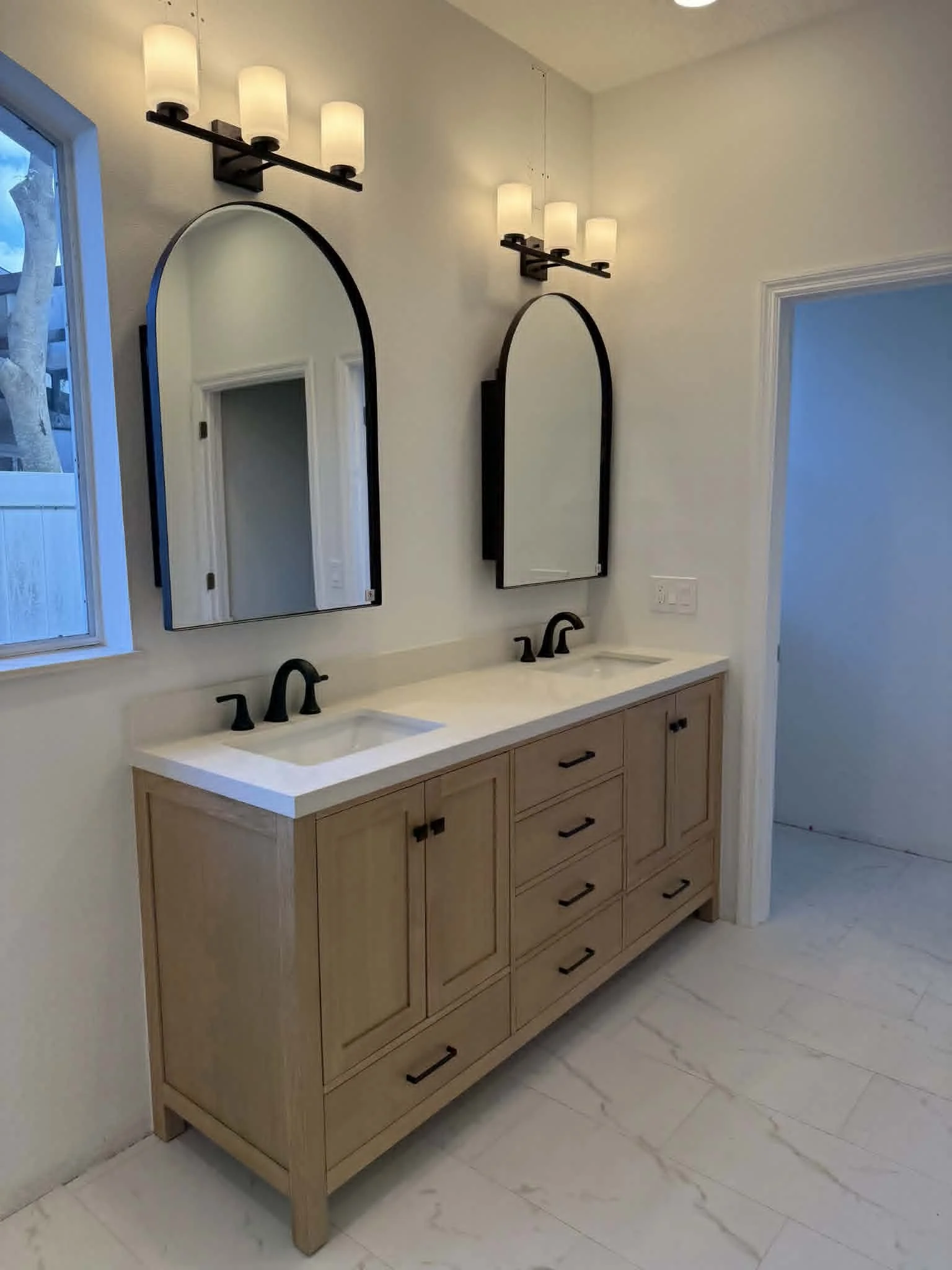 Modern Orlando bathroom remodel featuring custom dual vanity, quartz countertops, black fixtures, arched mirrors, upgraded lighting, and marble-look tile flooring.