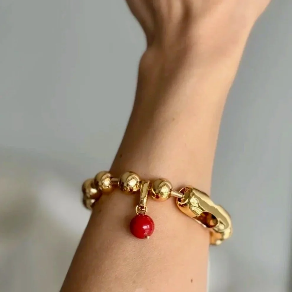 Gold bracelet with a red charm on a person's wrist.
