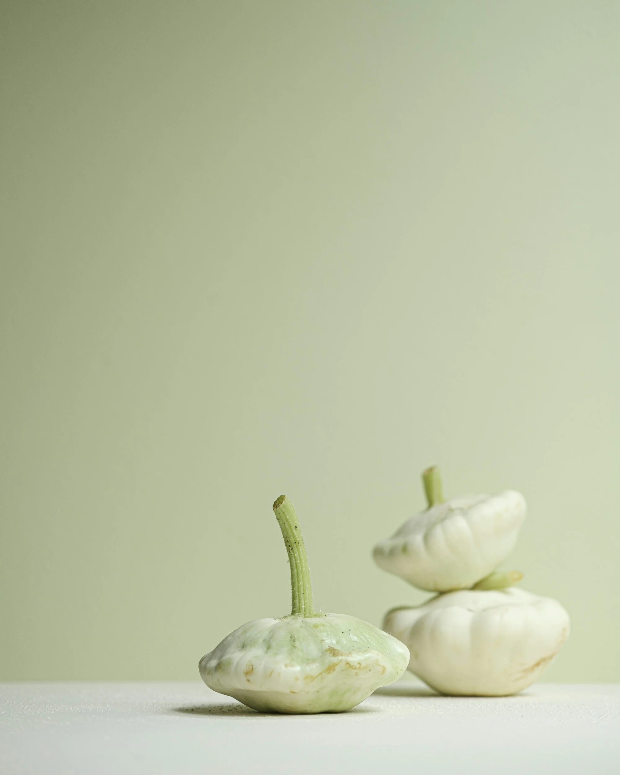Two white mushrooms with green stems on a white surface against a light green background.