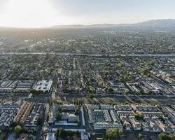 Aerial view of a cityscape with numerous buildings, streets, and a mountainous background under a bright sky.
