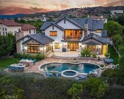 Luxury house with a backyard featuring a swimming pool and hot tub, surrounded by trees, with hills in the background at sunset