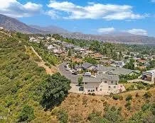 A view of a residential neighborhood with houses on a hillside, surrounded by trees and mountains in the background.