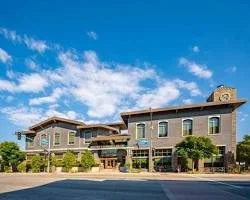 A large brick building with multiple stories, surrounded by trees, under a blue sky with some clouds.