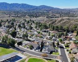 A suburban neighborhood with houses, trees, and a road, set against a mountainous background.