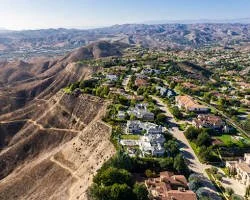 Aerial view of a suburban neighborhood along a hilly landscape with dry, rugged terrain and mountains in the background.