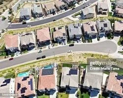 Aerial view of a neighborhood street with houses, cars parked along the curb, and a swimming pool in one yard