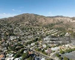 Aerial view of a city with residential houses and streets, set against a backdrop of mountains under a clear blue sky.