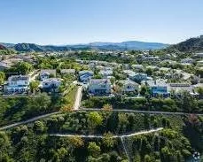 An aerial view of a residential neighborhood with houses, trees, and hills in the background under a clear blue sky.