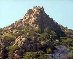 A rocky hill or small mountain with vegetation on its slopes, under a clear sky.