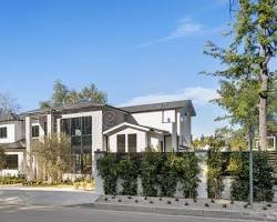 Modern two-story residential house with white and black exterior, surrounded by a fence and trees, under a blue sky.