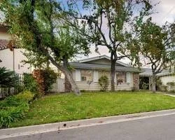 A house with beige siding, two stories, and a front yard with green grass and trees.